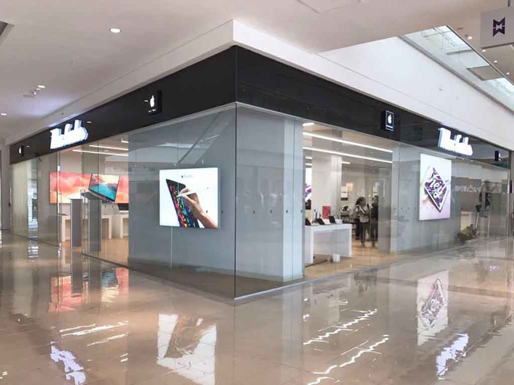 Vista exterior de una tienda Apple Store en un centro comercial que exhibe productos Apple y ofrece un entorno minorista de primera calidad.